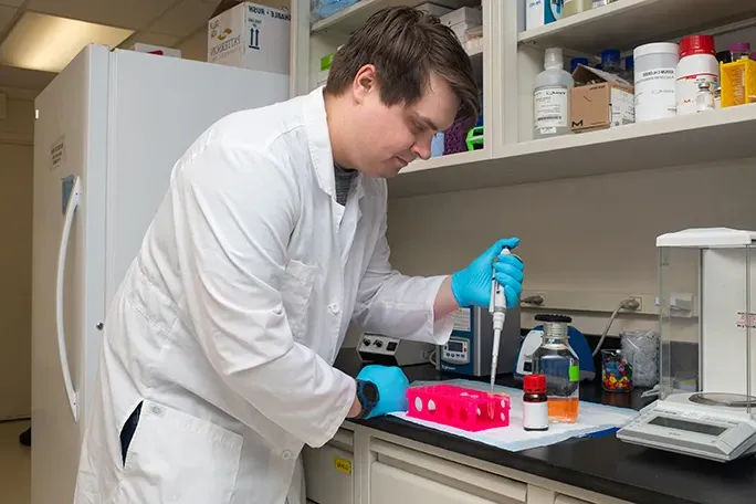 A student pipes a liquid into a container in a research lab